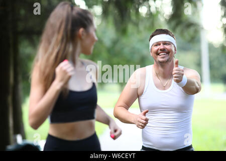 Fatty millennial man running in park with Stock Photo