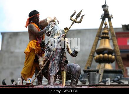 (190801) -- BEIJING, Aug. 1, 2019 (Xinhua) -- A Hindu priest pours milk to the idol of Lord Shiva at the Shiva temple in Kathmandu, Nepal, July 31, 2019. The holy month of Shrawan is considered auspicious by Hindus for praying to Lord Shiva for happiness and prosperity. (Photo by Sunil Sharma/Xinhua) Stock Photo