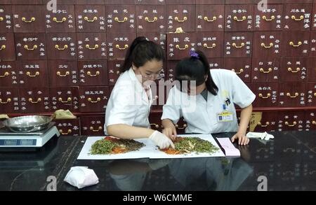 (190801) -- BEIJING, Aug. 1, 2019 (Xinhua) -- Photo taken with a mobile phone shows pharmacists preparing Chinese herbal medicine at a Chinese medicine store in Beijing, capital of China, July 31, 2019. (Xinhua/Zhang Chao) Stock Photo