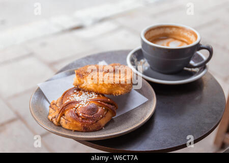 Cup of coffee and bun with cinnamon lying on the table in cafe Stock Photo