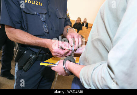 Kempten, Germany. 01st Aug, 2019. A policeman opens the handcuff of the 22-year-old defendant in the district court. Because he wanted to take revenge on his ex-girlfriend, who had separated a few weeks ago, the young man is said to have brutally beaten to death his son, who was only eight months old. Since today (01.08.2019) the father has to answer for murder before the district court of Kempten. Credit: Karl-Josef Hildenbrand/dpa/Alamy Live News Stock Photo