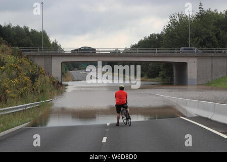 A bike rider comes to a halt as flood water blocks a road on the A555 near Handforth, Cheshire, where a major incident was declared late on Wednesday after heavy rainfall caused severe flooding. Stock Photo