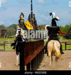 A knight in armour jousting with lance at the outdoor Medieval Centre in Nykøbing Falster, Denmark. The Medieval Centre is built around the village Sundkøbing at a fjord as it was around the year 1400. Houses are authentically designed and built with the people who populate the village, men, women, children, peasants, craftsmen, warriors and knights etc dressing and work as they would back in 1400.  Canons and large trebuchets can be seen firing missiles with knights in armour on horseback competing with lances and swords, dyers colour textiles with plants and in the convent garden nuns grow m Stock Photo
