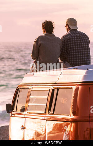 A couple sitting on top of their VW Volkswagen Campervan enjoying the evening light at Fistral in Newquay in Cornwall. Stock Photo