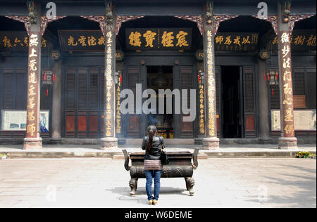 Chinese woman praying at Wenshu Temple, a Chinese Buddhist Temple in Chengdu. She holds an incense stick and stands in front of an incense burner. Stock Photo