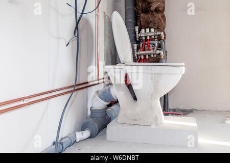 Closeup toilet on the block of aerated concrete on  floor against  background construction in bathroom, water copper and sewer gray pipes in isolation Stock Photo