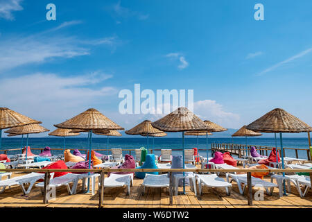 Beach umbrellas and colorful beach lounge chairs on a deck by the Aegean Sea in western Turkey Stock Photo