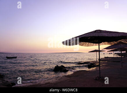 Bamboo sun umbrellas on the empty beach by the sea on the sunset, with pastel color sky and sea in a beautiful summer evening Stock Photo