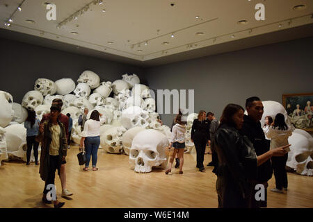 Visitors view 'Mass', an artwork of 100 larger-than-life skulls by Australian sculptor Ron Mueck, on display during the NGV Triennial art exhibition a Stock Photo