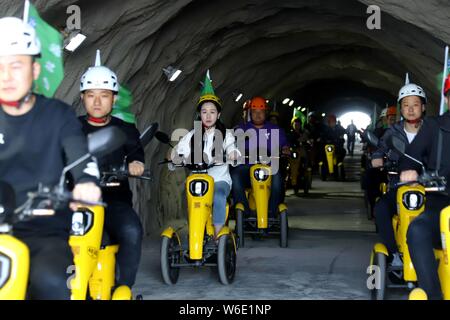 Volunteers ride electric bikes on a glass walkway along the edge of a ...