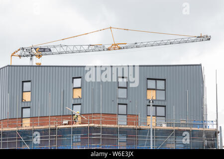 A tower block under construction with builders or construction workers working on scaffolding with a crane in the background Stock Photo