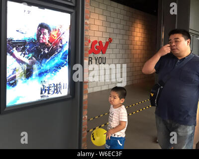 --FILE--Chinese film goers walk past a poster of the Chinese action movie "Wolf Warriors 2" displayed at a cinema in Shanghai, China, 19 August 2017. Stock Photo