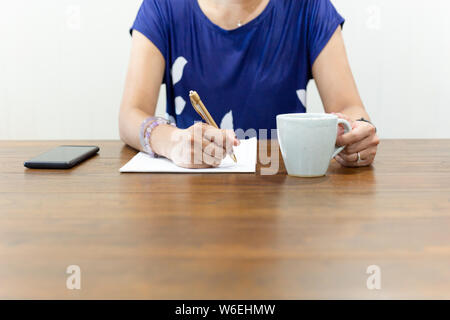 Businesswoman hand writing on paperwork with cup of coffee on working desk. Stock Photo
