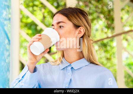Young and attractive woman drinking coffee from coffee eco biodegradable cup at modern park. Eco friendly take away mug. Stock Photo