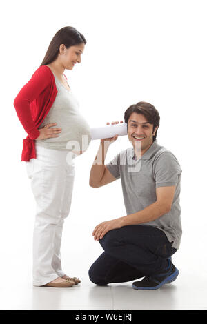 Man listening to pregnant woman,s stomach through rolled up paper Stock Photo