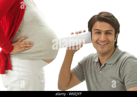 Man listening to pregnant woman's stomach through rolled up paper Stock Photo