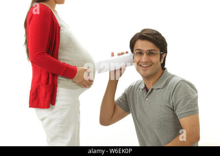 Man listening to pregnant woman's stomach through rolled up paper Stock Photo