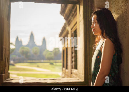 Candid portrait of brunette Asian solo female traveler with in Siem Reap, Cambodia. There's a famous Angkor Wat temple in the background. Stock Photo