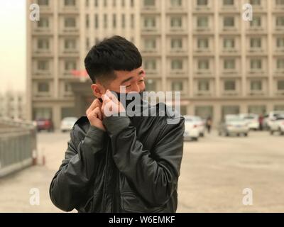 A local resident tries to cover his mouth in a sandstorm in Xilinhot city, north China's Inner Mongolia Autonomous Region, 27 March 2018.   A huge san Stock Photo