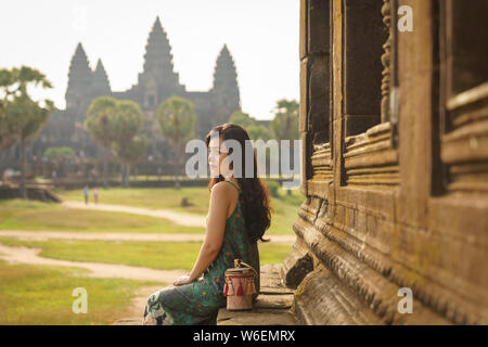 Candid portrait of brunette Asian solo female traveler with in Siem Reap, Cambodia. There's a famous Angkor Wat temple in the background. Stock Photo