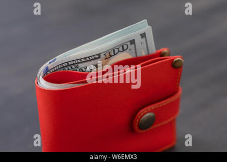 Money sticking out of a red leather wallet on a dark blurry background. Symbol of good luck, increasing the amount of money. Stock Photo