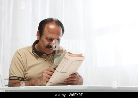 Old man reading newspaper with magnifying glass Stock Photo