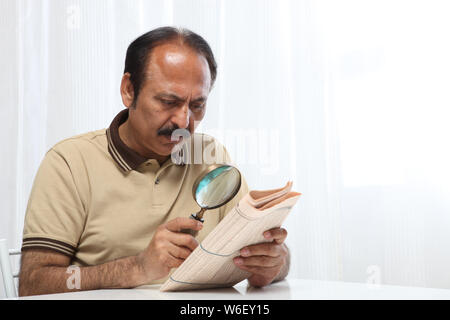Old man reading newspaper with magnifying glass Stock Photo