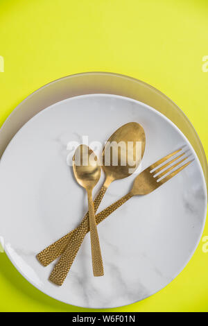 Top view of place setting with plate, knife and fork isolated on yellow background.Vintage gold knife, fork, spoon and plate.Dinner place setting.Copy Stock Photo
