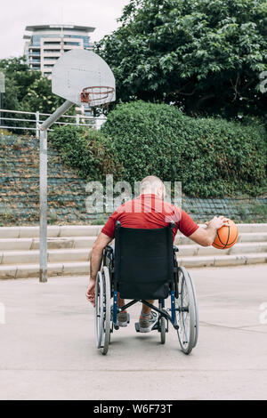 disabled man in wheelchair playing basketball alone in the city, concept of adaptive sports and physical activity, rehabilitation for people with phys Stock Photo