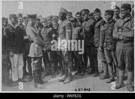 Americans in German prison camp. A group of American prisoners in a German prison camp listening at . . .; Scope and content:  The full caption for this item is as follows: Americans in German prison camp. A group of American prisoners in a German prison camp listening attentively while a jovial [African American] fighter relates an episode of war life to a German officer. Stock Photo