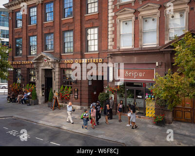 London, United Kingdom – August 13, 2017: Streetlife with people walking around in front of The Hung, Drawn and Quartered pub and Sripur Restaurant in Stock Photo