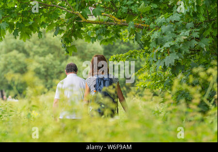 A couple walking through a country path in the countryside on a hot day in Spring in the UK. Stock Photo