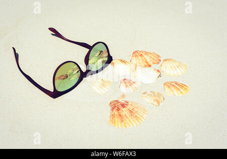 sunglasses on the sand with seashells, tropical sea background Stock Photo