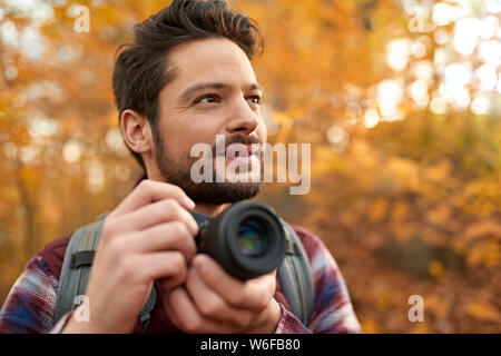 Attractive caucasian man taking pictures with a mirrorless camera through the forest in the fall in Canada Stock Photo