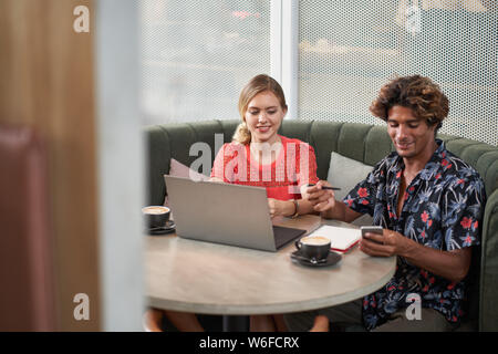 Candid lifestyle shot of male and female millennial colleagues brainstorming at table of bright modern tropical cafe Stock Photo