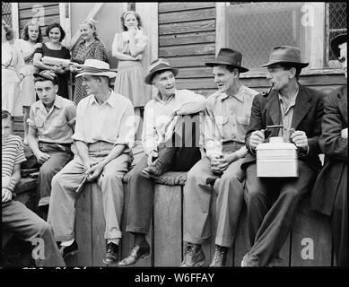 Blaine Sergent, with pulled-up leg, talks with his miner friends on the front porch of the company store on a Saturday pay-day morning. P V & K Coal Company, Clover Gap Mine, Lejunior, Harlan County, Kentucky. Stock Photo