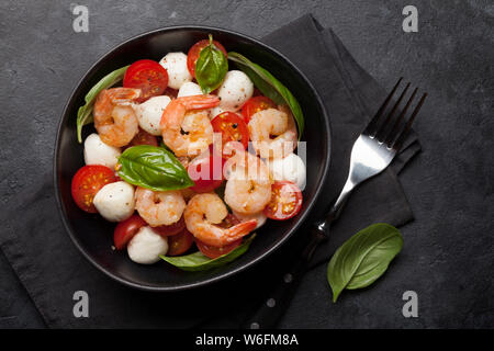 Fresh caprese salad with cherry tomatoes, mozzarella, basil leaves and grilled shrimps. Flat lay. Top view Stock Photo