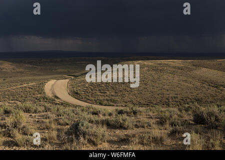 A dirt road winds through the sagebrush shrubland in Wyoming as a storm approaches. Stock Photo