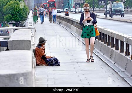 London, England, UK. Homeless man begging on Waterloo Bridge, young woman walking past Stock Photo