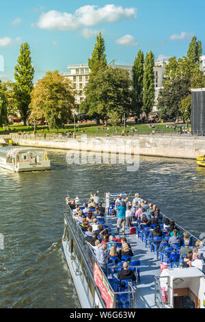 BERLIN, GERMANY - SEPTEMBER 26, 2018: Colorful picture of a tourist boat with intense blue chairs going down the Spree river, with people walking in Stock Photo