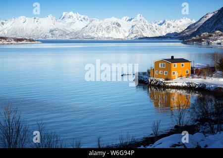 traditional norwegian wooden house to stand at the lakeside and mountains in the distance. Lofoten Islands. Norway. Stock Photo