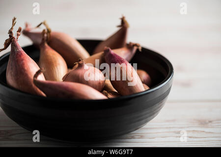 Banana and round shallots in a dark bowl on a wooden table, negative space Stock Photo