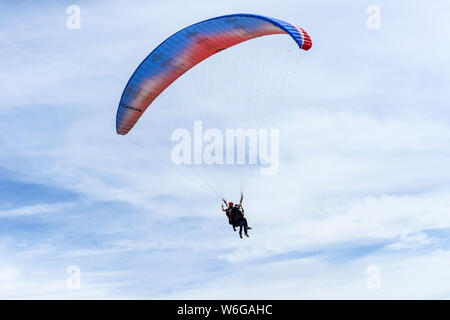 Flying In Clouds - A tandem paraglider soaring high in white clouds of blue sky above Lookout Mountain near city of Golden, Colorado, USA. Stock Photo