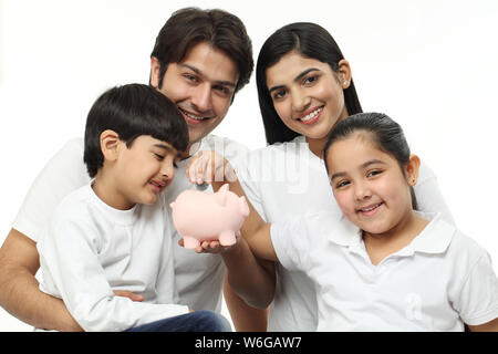 Girl putting coin into a piggy bank with their family Stock Photo