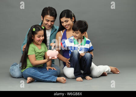 Boy putting coin into a piggy bank with their family Stock Photo