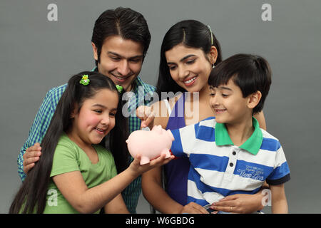 Boy putting coin into a piggy bank with their family Stock Photo