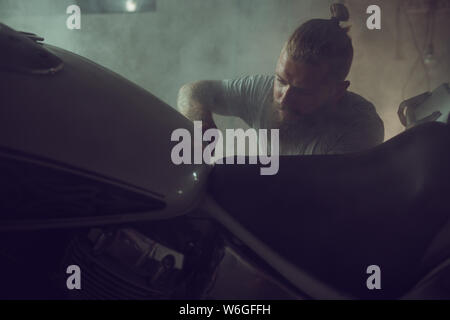 Handsome brutal man with a beard repairing a motorcycle in his garage. Stock Photo