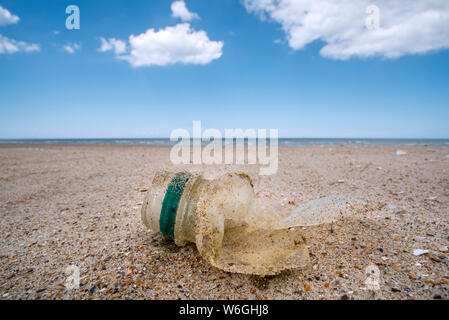 Old partly broken down plastic bottle, non-biodegradable waste washed ashore on sandy beach along the North Sea coast Stock Photo