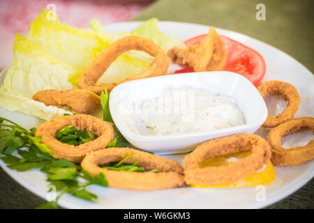 Tasty squid rings in bread flour. Squid is served with greens sauce and fresh greens with tomatoes and lettuce. Stock Photo
