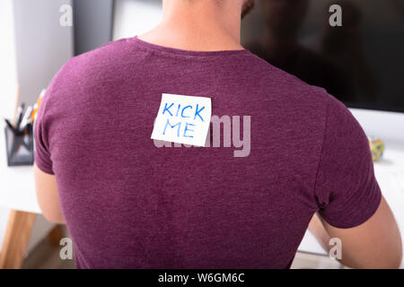 Rear View Of Man Working In Office With Kick Me Text Written On Sticky Note Stock Photo